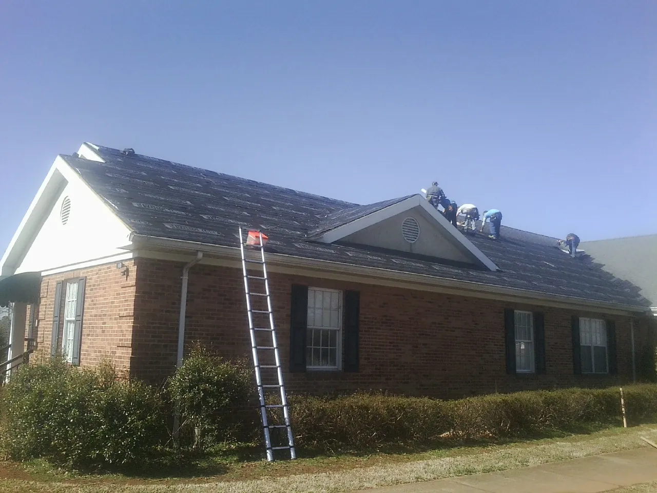 Crew tearing shingles off a brick ranch roof with a ladder set — Metal Roof Repair work by our crew in Akron