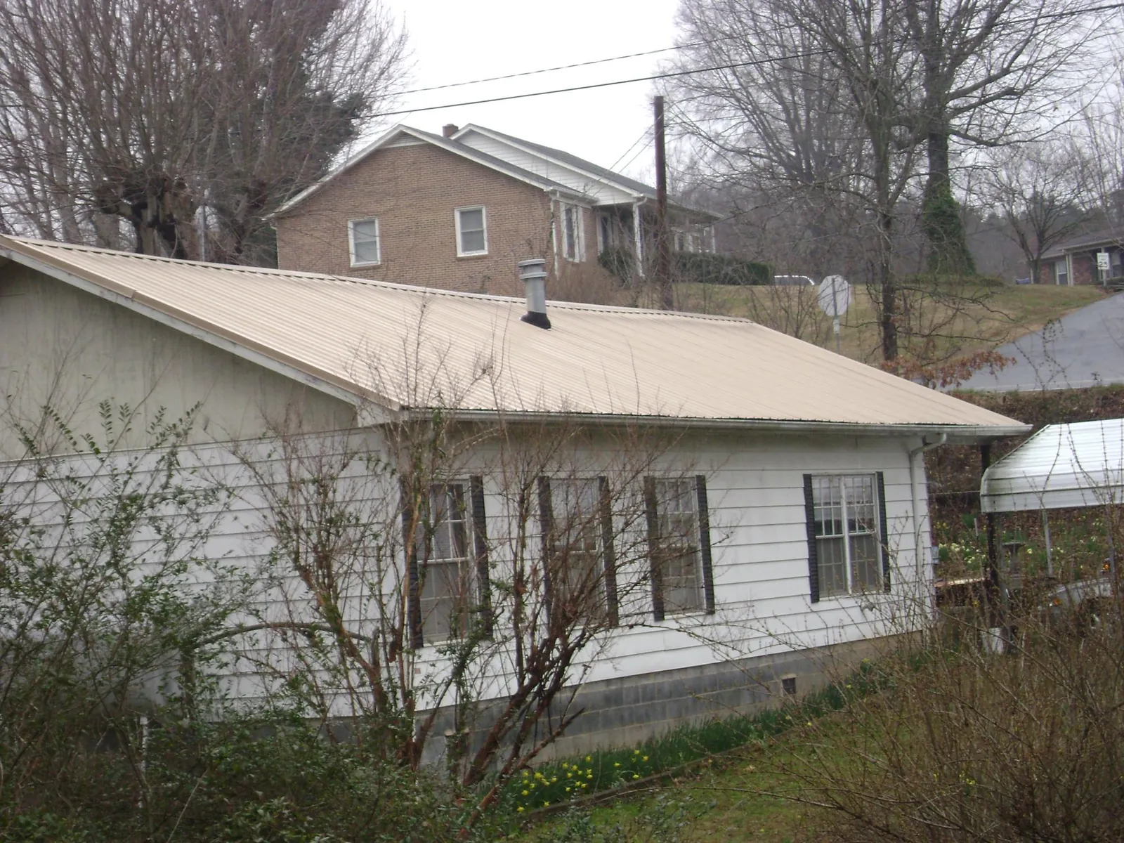 Tan metal roof on a white sided house set into a hillside — Commercial Roofing by Roofing Brothers in Akron